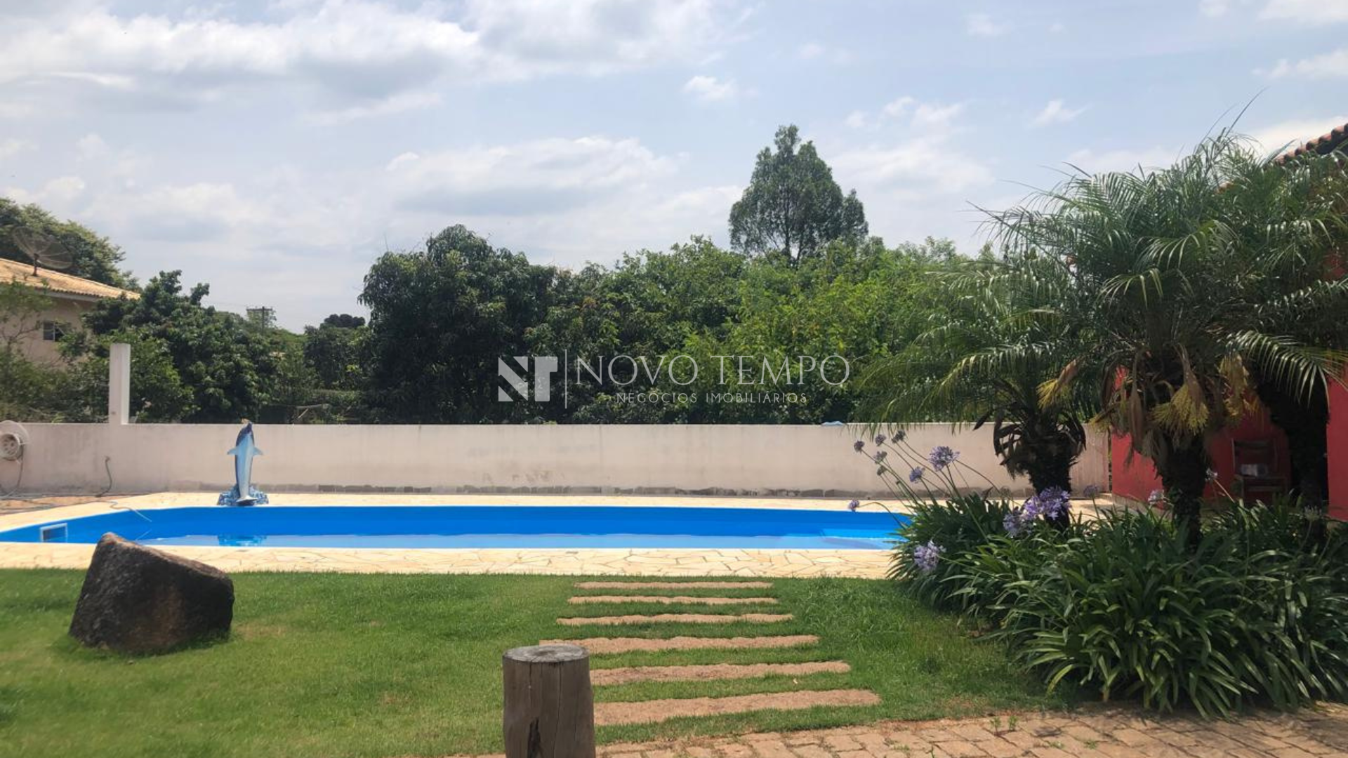 Fachada da chácara à venda no Bairro Pinhal IV, Cabreúva — arquitetura residencial e jardim; Sala com três ambientes e lareira na chácara em Cabreúva; Suíte da casa principal na chácara do Pinhal IV; Cozinha planejada da casa principal — integração e funcionalidade; Salão com churrasqueira e cozinha americana no anexo — ideal para eventos; Piscina com cascata em chácara à venda em Cabreúva; Pomar e lago na área externa da chácara — natureza e lazer; Córrego nos fundos da propriedade — privacidade e paisagismo; Canil e galinheiro na chácara — infraestrutura para animais; Vista aérea do terreno de 2.293,10 m² no Bairro Pinhal IV, Cabreúva.